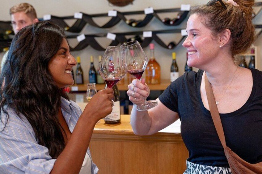 Two people holding wine glasses in a bar with wine bottles in the background. 2