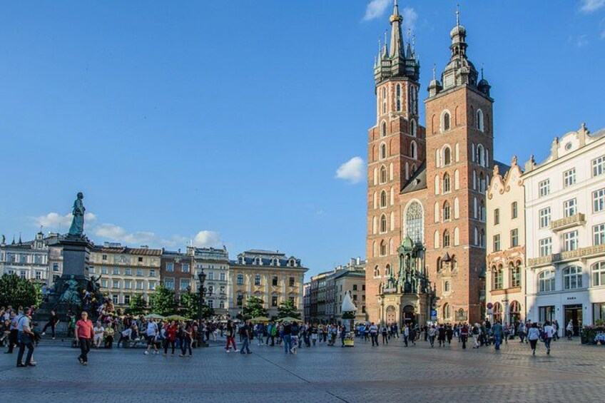 A bustling square with a prominent church featuring twin towers and a statue in the foreground. 1