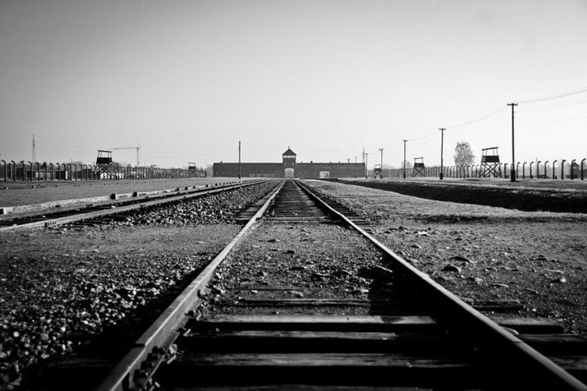 Railway tracks leading to a distant building, surrounded by a fence and utility poles. 3