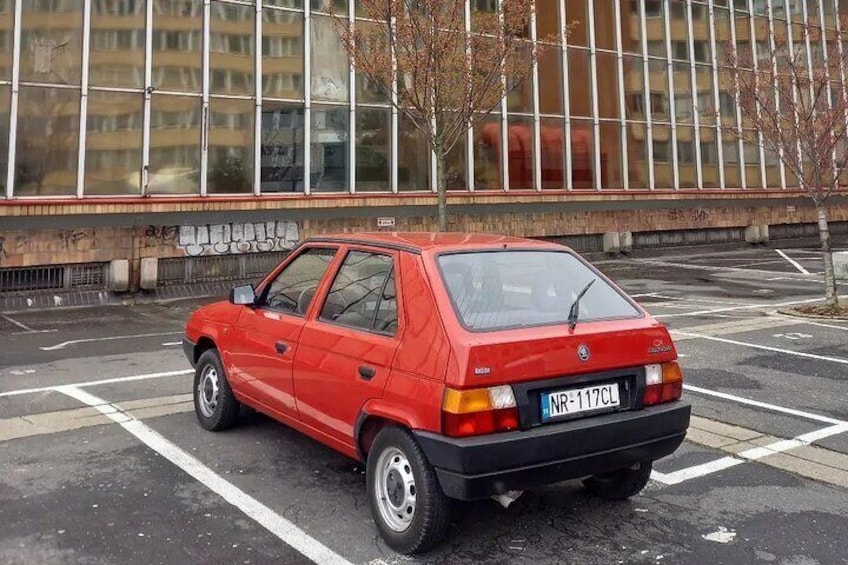 Une voiture rouge est garée sur un parking, avec un bâtiment en arrière-plan. 2