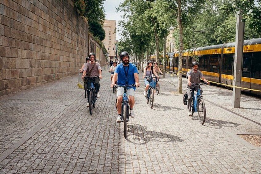 Des personnes à vélo circulent sur une rue pavée, avec un train en arrière-plan. 2