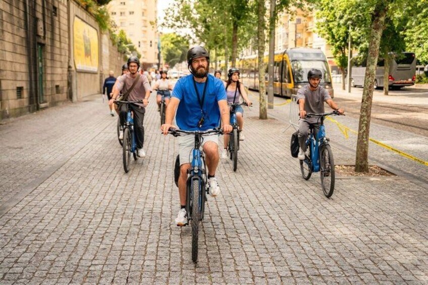 Un gruppo di ciclisti su una strada acciottolata, con edifici e alberi sullo sfondo. 3