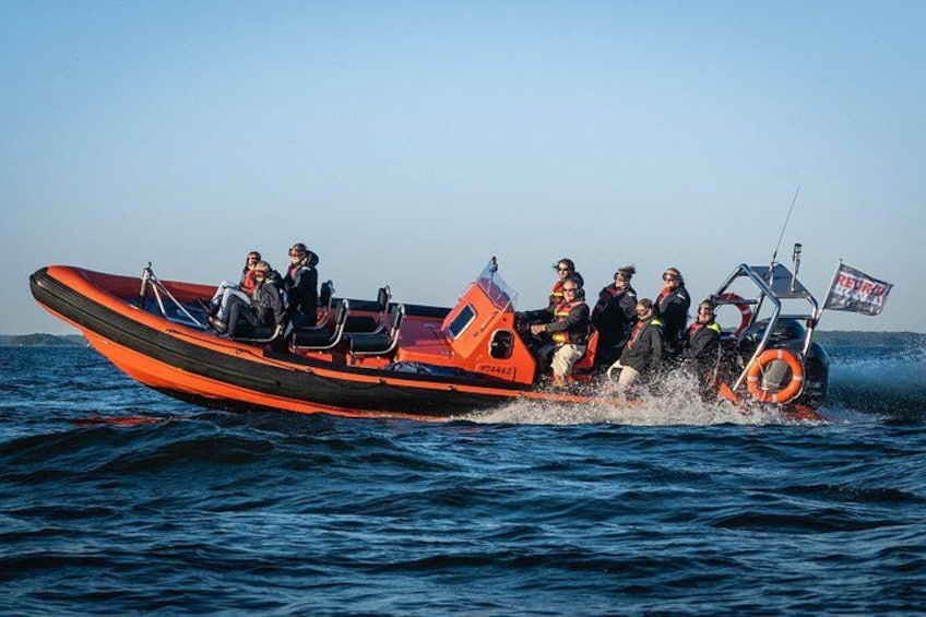 A group of people on a small orange boat with a flag, moving through the water. 1