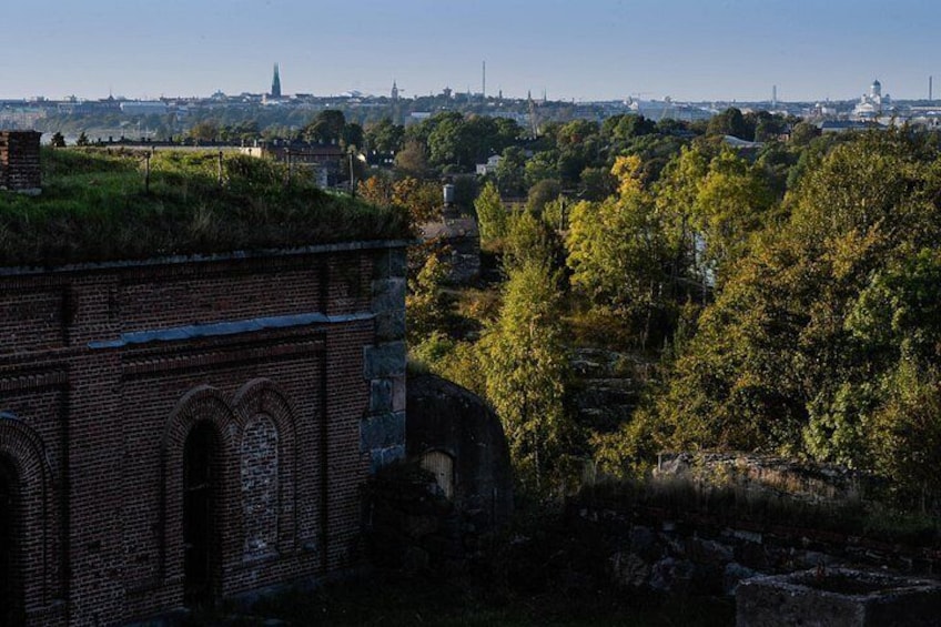 A brick building with arched windows, surrounded by trees and a distant city skyline. 4