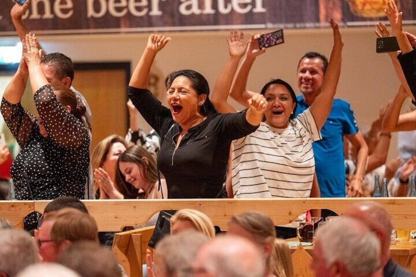 A group of people cheering at an event, with a sign reading "the beer after" in the background. 2