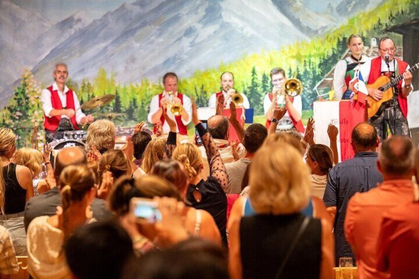 A brass band performing on stage with a mountainous backdrop. 3