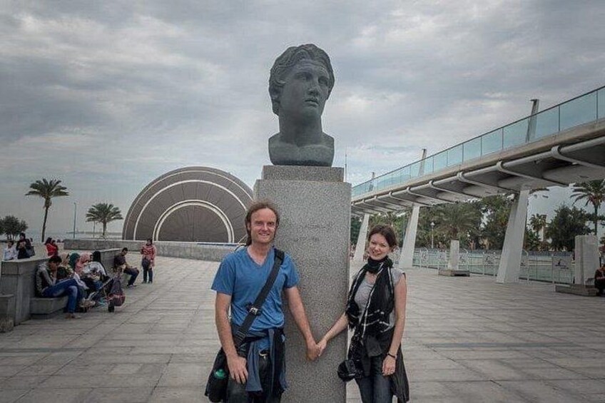 Een stel staat voor een sculptuur, met een moderne brug en palmbomen op de achtergrond. 5