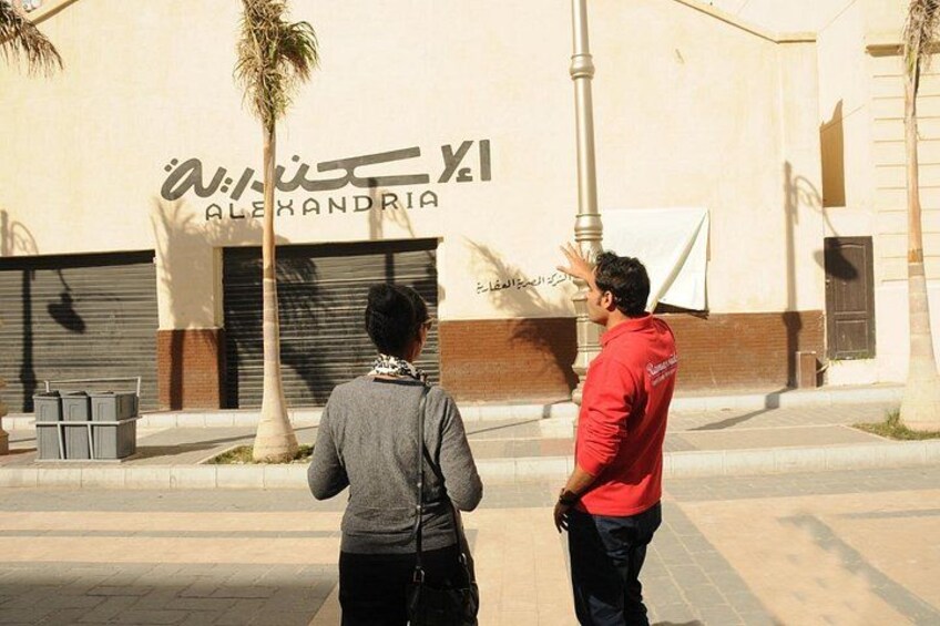 Two people standing in front of a building with a sign that reads 'Alexandria.' 4