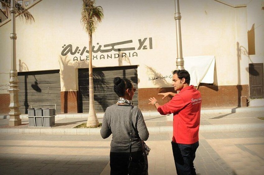 Two people standing in front of a building with Arabic signage. 2