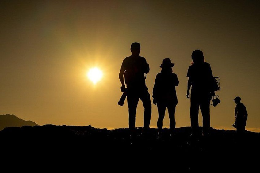 Silueta de cuatro personas de pie en una colina, con el sol poniéndose al fondo. 3