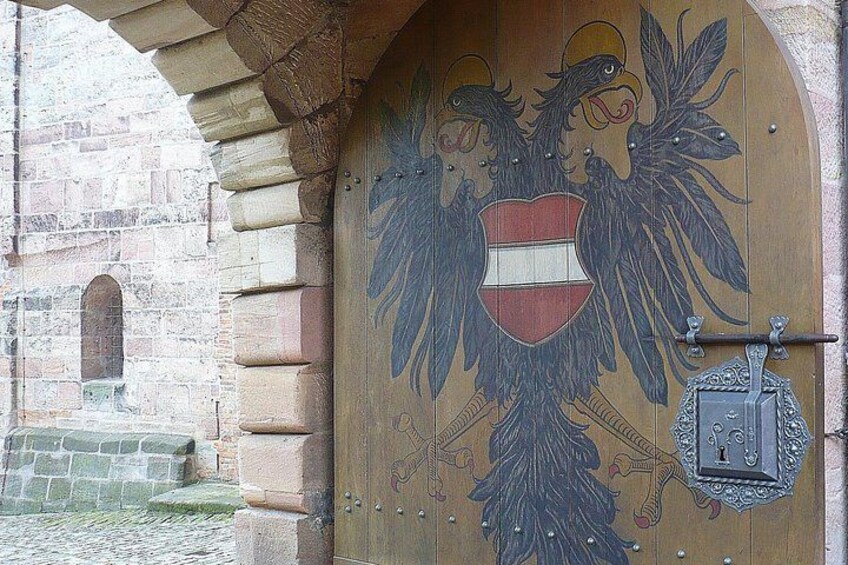 Una puerta de madera con un emblema de águila y un escudo, enmarcada en un arco de piedra. 2