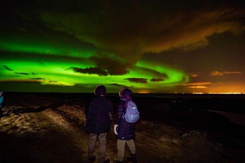 Two people standing on a sandy beach, gazing at the northern lights. 1