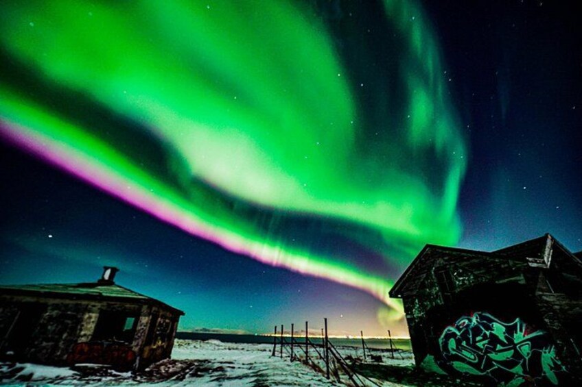 Paesaggio innevato con una casa e un edificio con graffiti, sotto un cielo notturno illuminato dall'aurora boreale. 1