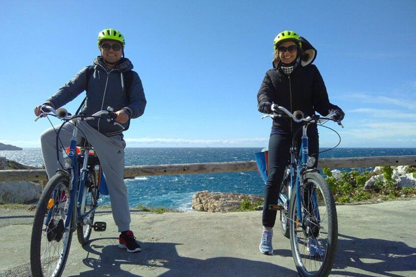 Two people on bicycles by a coastal road with the ocean in the background. 3