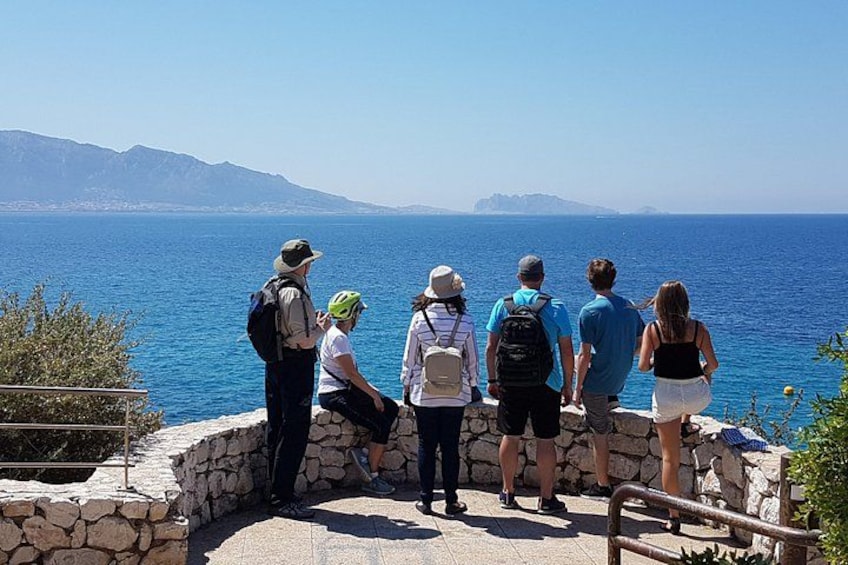 A group of people on a stone platform overlooking a body of water with mountains in the distance. 2