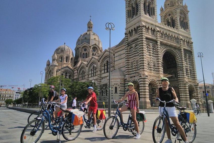 A group of people on bicycles in front of a large, ornate building with domes and towers. 1