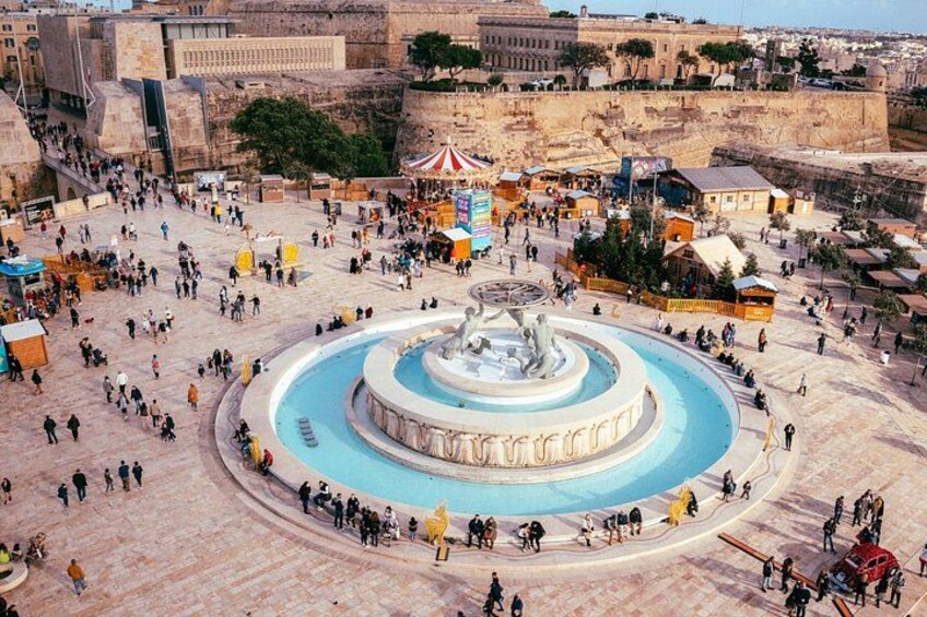 A public square with a central fountain, surrounding buildings, and a distant view of a fortified structure. 4