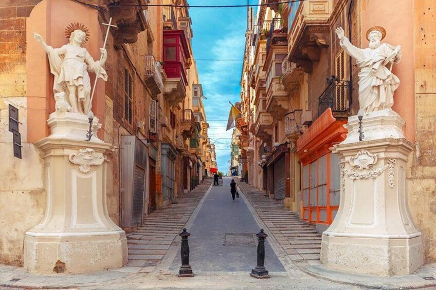A narrow street flanked by buildings with statues and balconies. 3