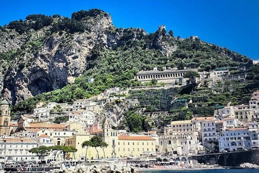 Un borgo costiero con edifici su una collina, una chiesa imponente e un castello in cima alla montagna. 2