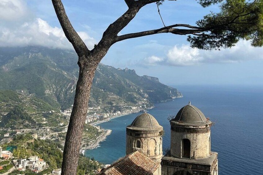 A coastal landscape with a view of the sea, a tree in the foreground, and two domed structures. 5