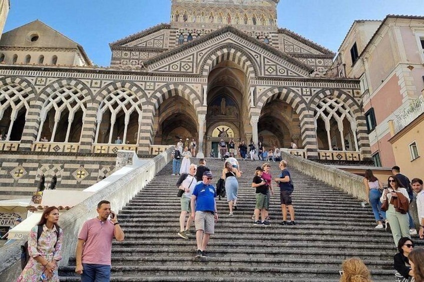 A historic building with intricate architecture, a staircase leading to its entrance, and people walking around. 2