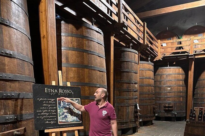 A man pointing at a signboard in a cellar with wooden barrels. 5
