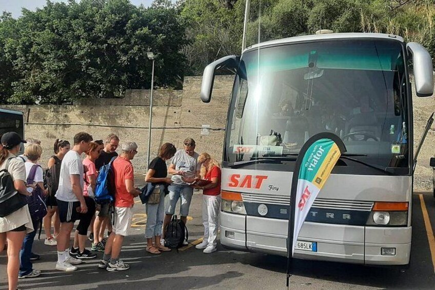 Un gruppo di persone in piedi davanti a un autobus con l'etichetta 'SAT' sulla parte anteriore. 2