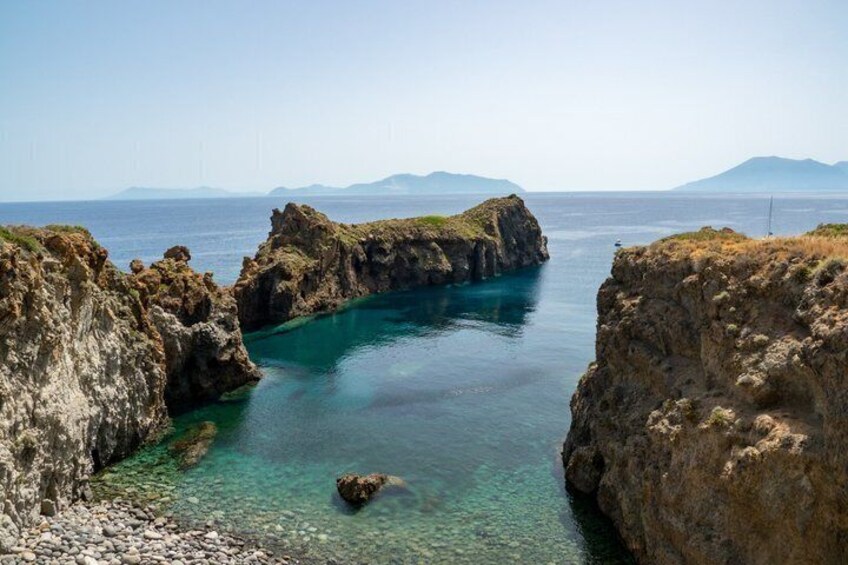 A coastal landscape with rocky cliffs, clear turquoise water, and distant mountains. 5