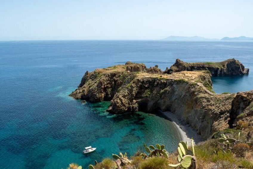 A coastal landscape with clear blue waters, rocky cliffs, and a boat near the shore. 4