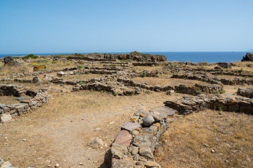 Ancient ruins with stone walls and pathways, a clear sky, and the sea in the background. 3