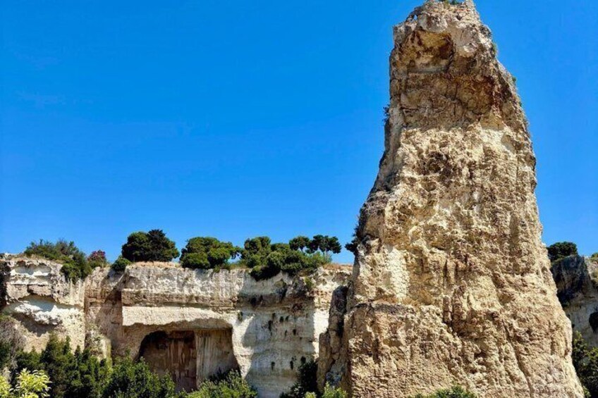 A rocky cliff with a cave entrance and a tall rock formation. 2