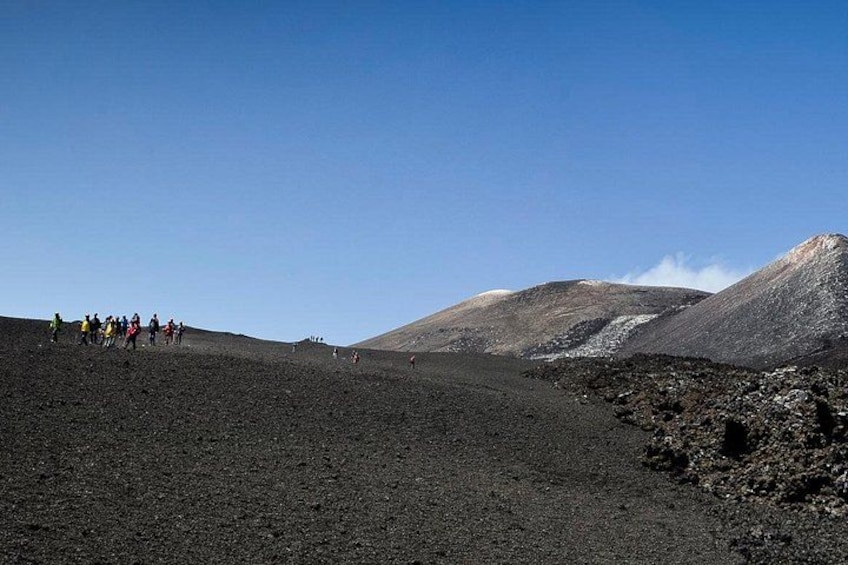 Un gruppo di persone che fa un'escursione su un terreno vulcanico sotto un cielo sereno. 2
