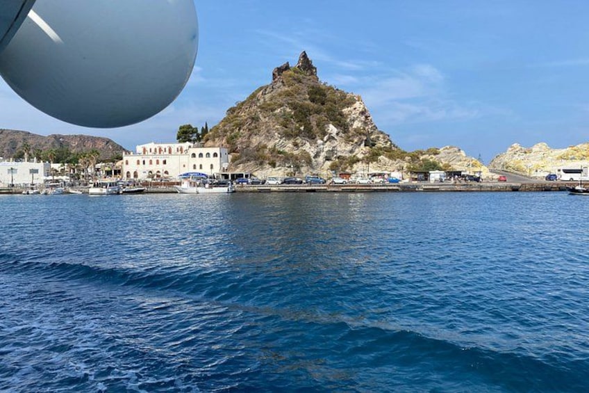 A coastal town with a prominent rocky hill, calm sea, and buildings along the shore. 2