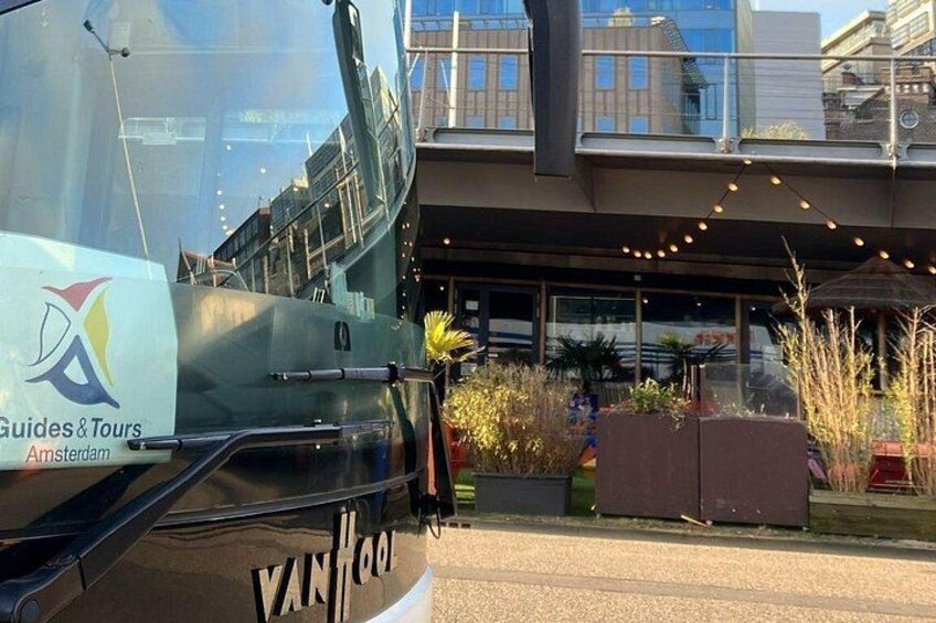 Un bote con la inscripción 'Guides & Tours Amsterdam' y 'VAN HOO', amarrado cerca de un edificio con luces colgantes. 2