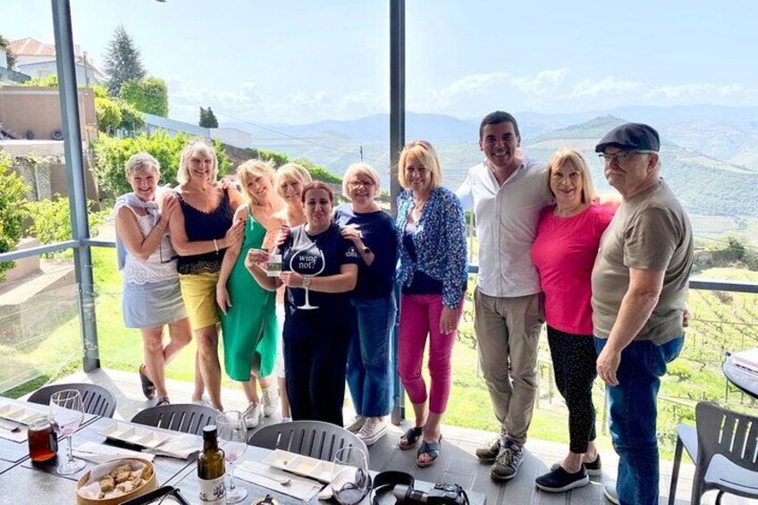 A group of people standing on a terrace with a scenic view of hills and a clear sky. 3