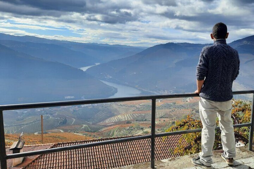 Un homme se tient sur un balcon qui donne sur une vallée, avec une rivière et des montagnes en contrebas. 2