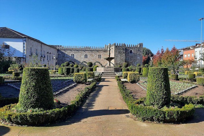 A pathway leading to a historic building with a tower, surrounded by well-manicured gardens and a clear blue sky. 4