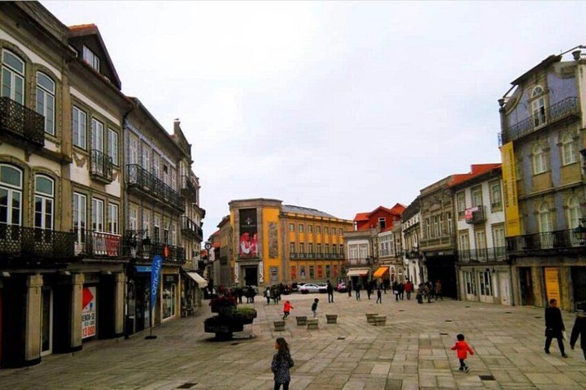 A plaza with historic buildings, a central fountain, and people walking. 4