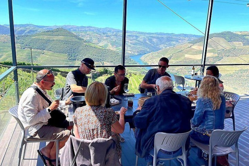 A group of people seated at a table with a scenic view of hills and a river. 4