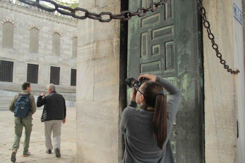 Una persona tomando una foto con una cámara, una cadena y un edificio con ventanas de arco en el fondo. 3