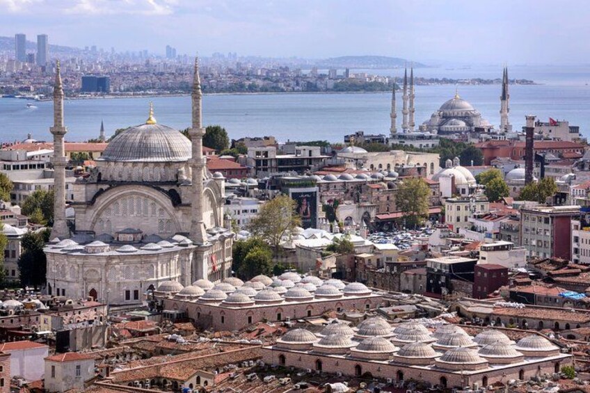 Un paisaje urbano con edificios de cúpulas destacadas, una gran mezquita con minaretes y una masa de agua al fondo. 2