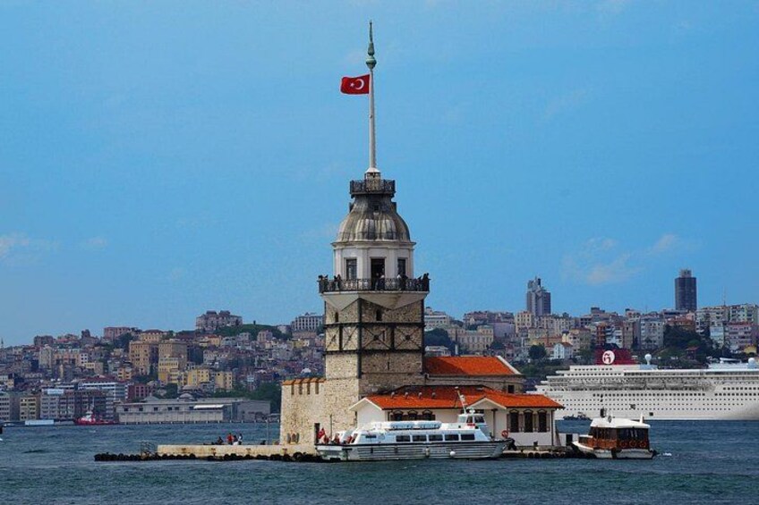 A historic tower with a flag, a cruise ship, and a cityscape in the background. 4