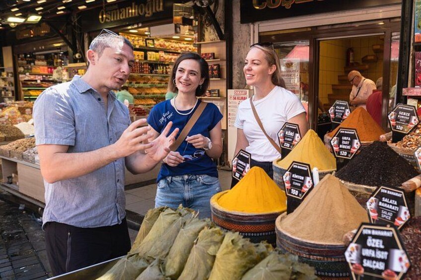 Trois personnes se trouvent sur un marché aux épices, devant un étalage où sont présentées différentes sortes d’épices. 1