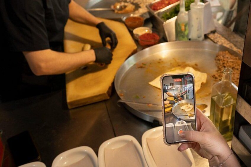 Iemand maakt een foto van een kookscène, met een grote metalen pan en diverse ingrediënten. 4