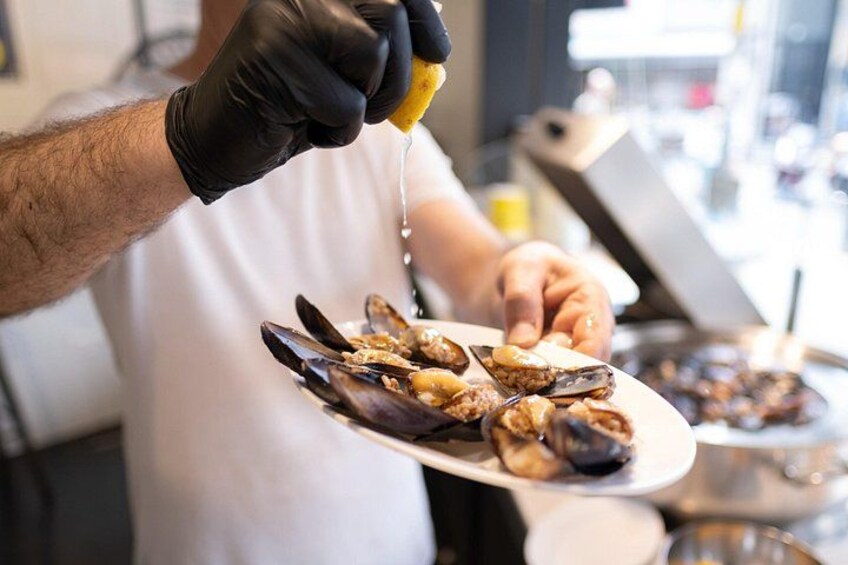 A person wearing gloves holding a plate of mussels. 3
