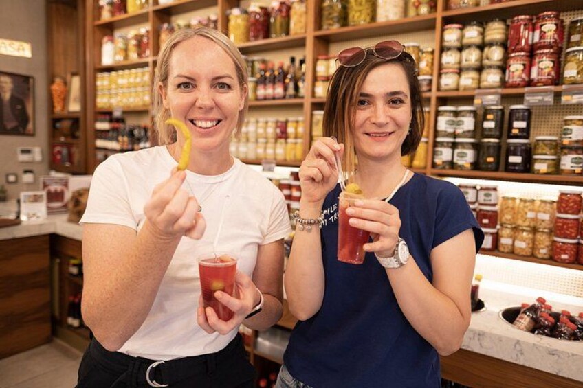 Twee personen houden etenswaren vast in een winkel, met in de achtergrond schappen vol potjes en flessen. 5