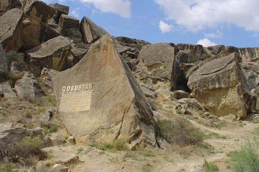 A rocky landscape with a large boulder labeled 'QOBUSTAN' and a narrow path. 1