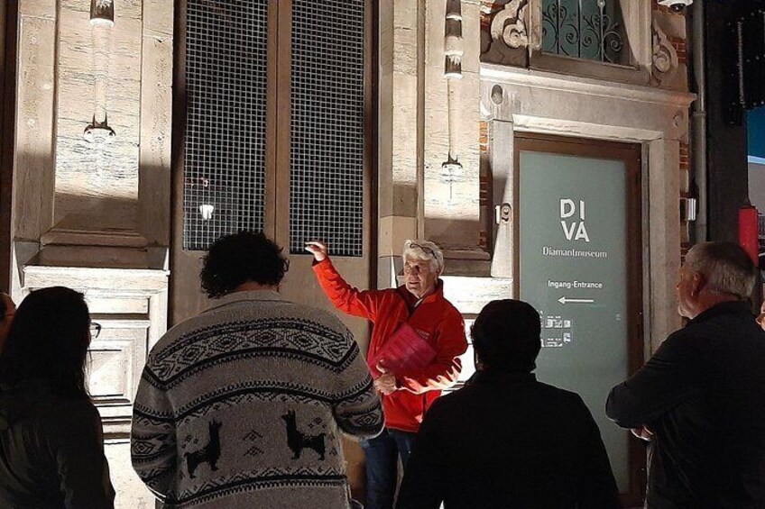 En person i en rød jakke peger på et skilt med teksten 'DI AVA' og 'Indgang-Entrance' i en bygning med klassisk arkitektur. 3