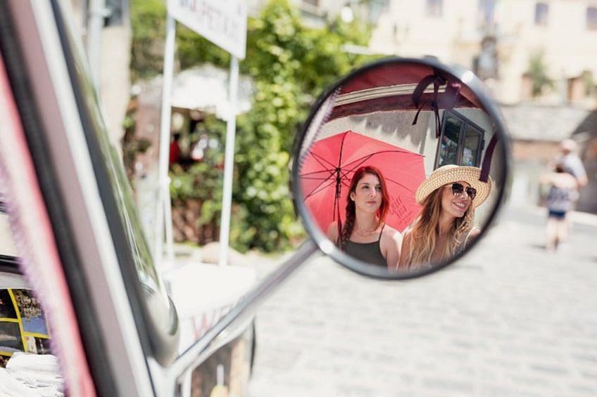 Nebenspiegel eines Autos, der zwei Personen zeigt: eine mit einem roten Regenschirm und die andere mit einem Strohhut. 5