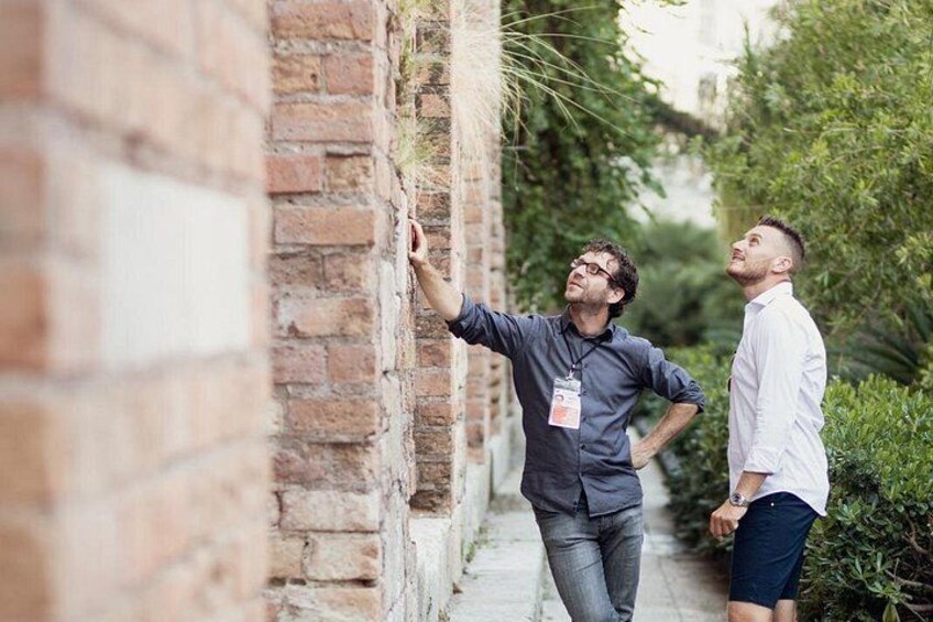 Dos personas caminando a lo largo de un muro de ladrillo con follaje al fondo. 3